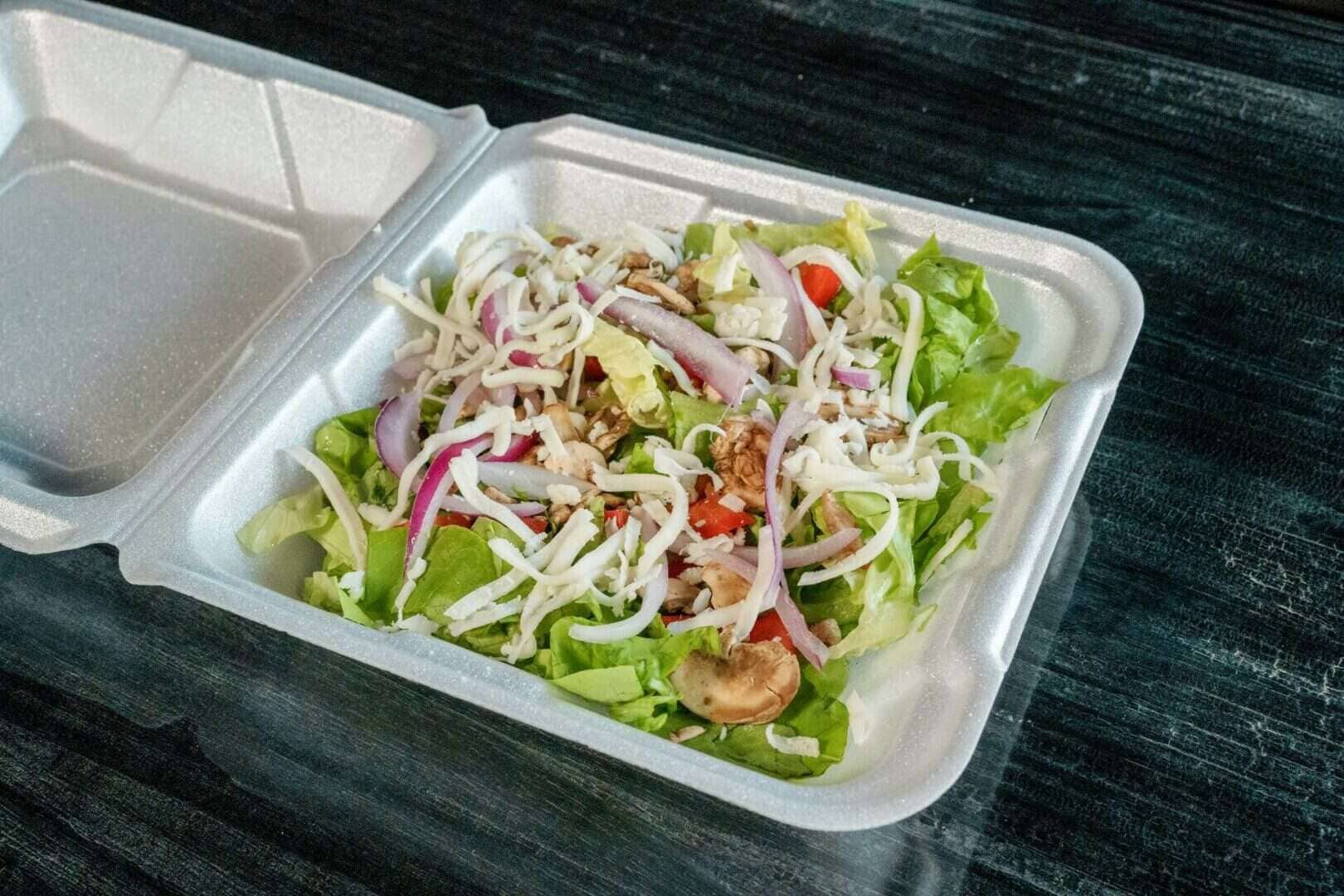 Fresh garden salad with lettuce, tomatoes, onions, and shredded cheese in a foam container.