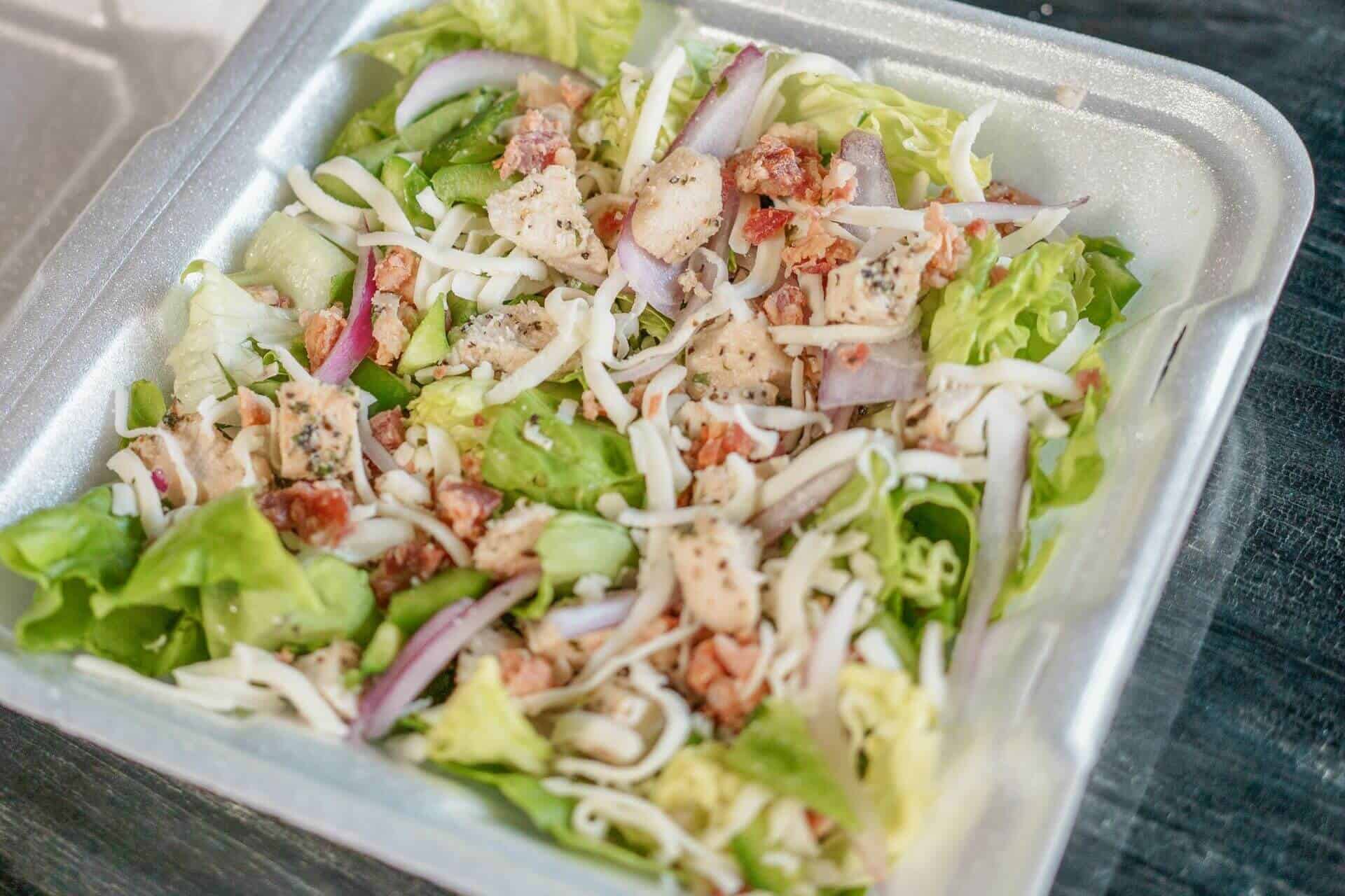 Fresh mixed salad with lettuce, onions, and chicken in a takeout container.