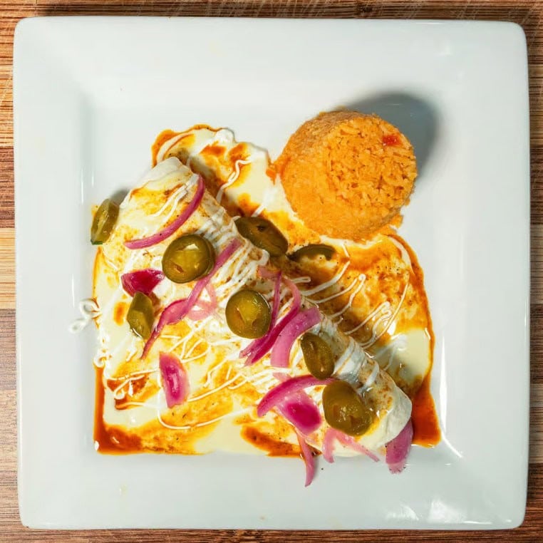 Fresh fish fillet topped with pickles, red onions, and lemon slices on a white plate.