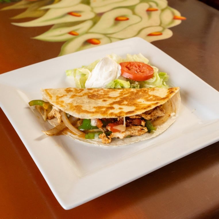 Delicious chicken quesadilla with melted cheese, served with fresh salad and tomato slices on a whit.