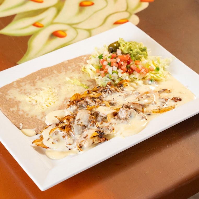 Chicken fajitas served with sautéed vegetables, melted cheese, and fresh salsa on a white plate. Per.
