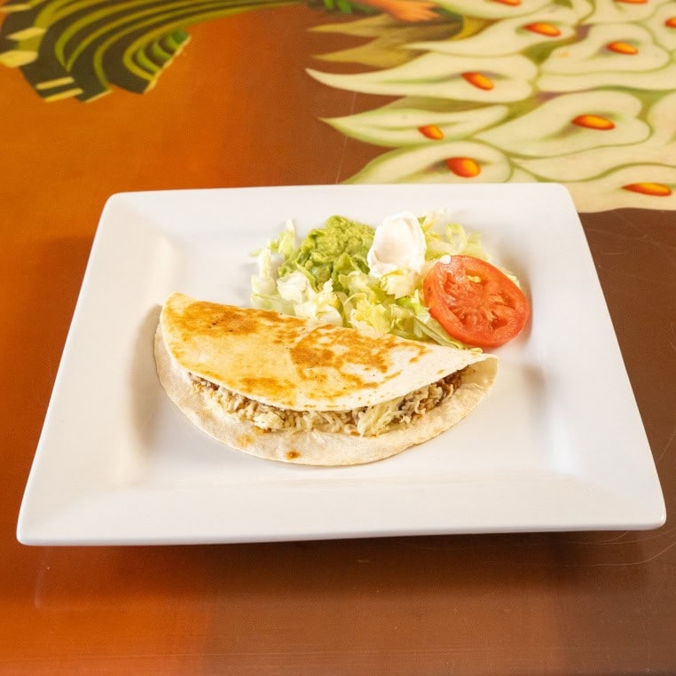 Grilled chicken quesadilla served with fresh salad and tomato slice on a white plate.