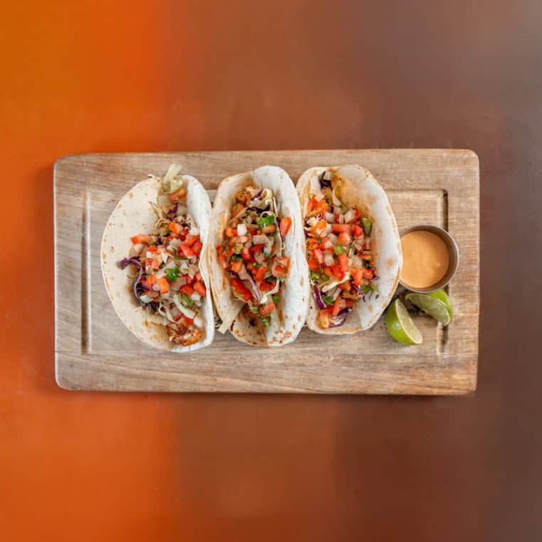 Delicious tacos topped with fresh salsa, served with lime and a side of sauce on a wooden platter. P.