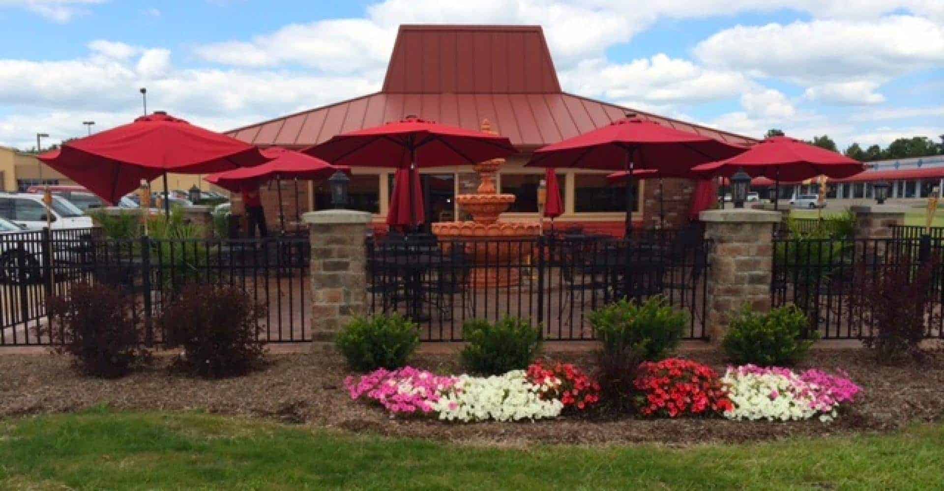 Outdoor restaurant patio with red umbrellas and garden flowers.