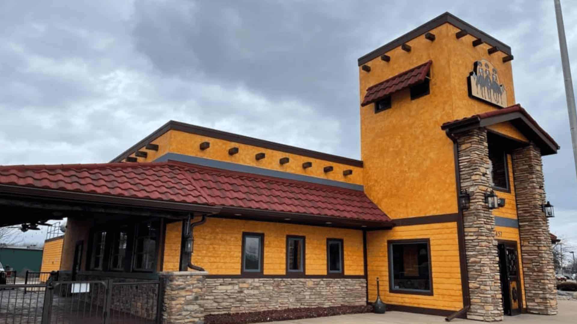 Exterior view of a colorful, modern restaurant building with a yellow and orange facade, stone accen.