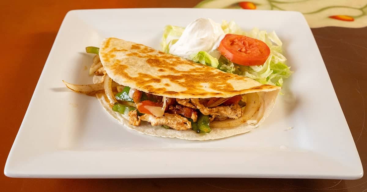 Delicious chicken taco with fresh lettuce, tomato, and creamy sauce on a white plate.