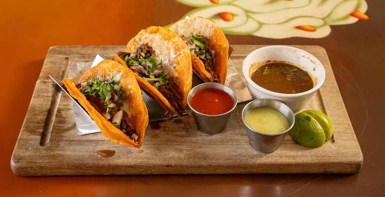 Delicious tacos with fresh ingredients, salsa, and lime on a wooden serving board.