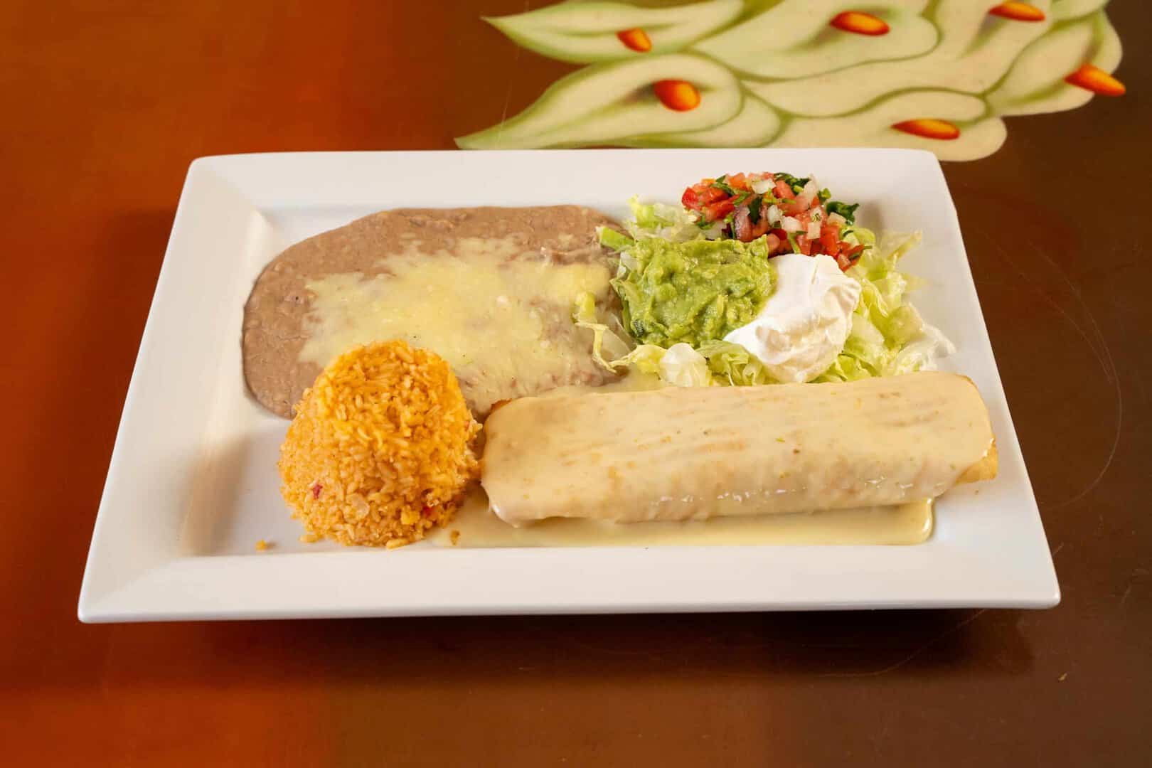 Chicken enchilada with melted cheese, rice, and fresh guacamole on a white plate.