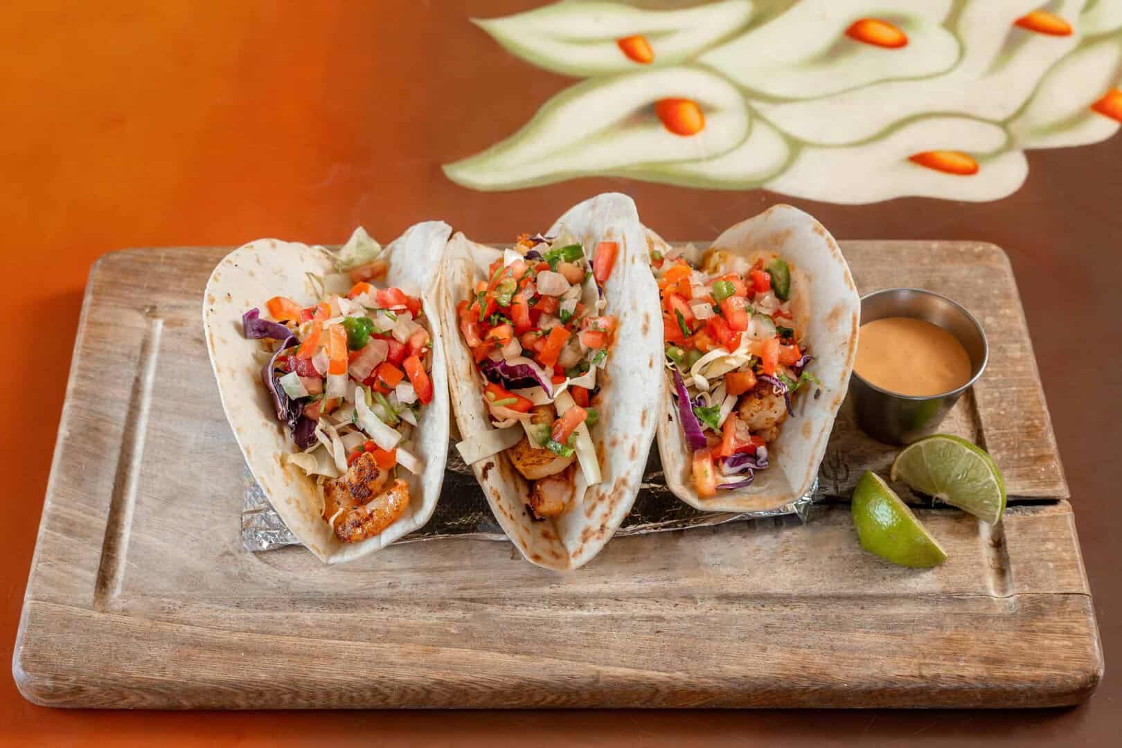 Delicious chicken tacos with fresh salsa served on a wooden platter with lime wedges and sauce.