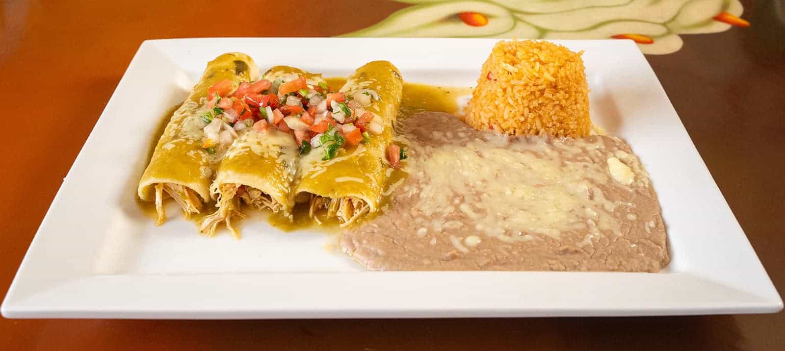 Enchiladas served with flavorful rice and beans, topped with fresh salsa and melted cheese on a whit.