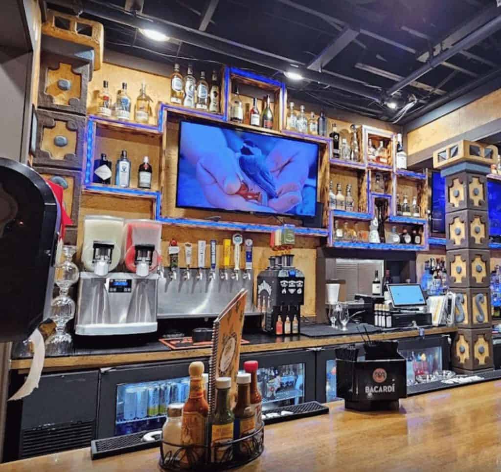 Stylish bar setup featuring liquor bottles, beverage dispensers, and a digital screen for entertainm.