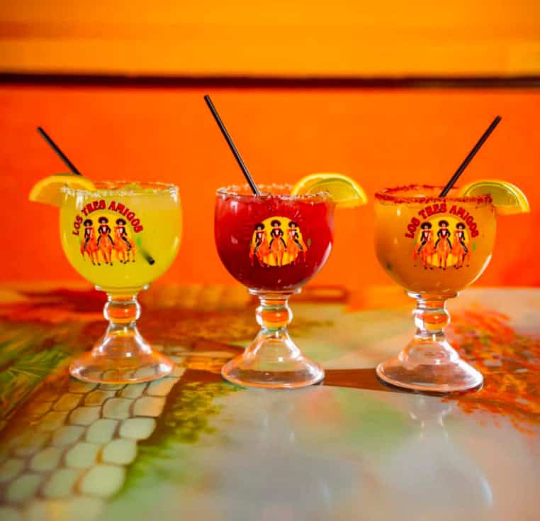Colorful tropical fruit cocktails served in branded glasses with lemon slices.