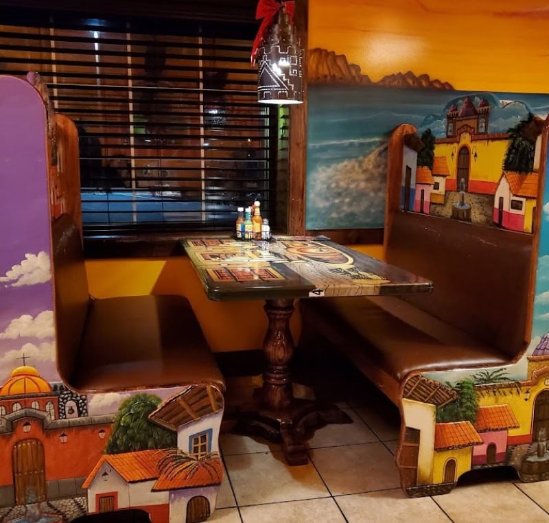 Cozy restaurant booth with colorful mural of a seaside village, creating a welcoming atmosphere for.