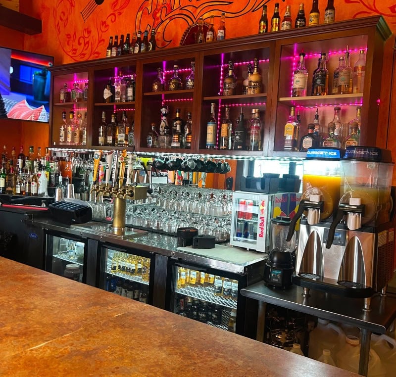 Bar counter with bottles, glasses, and coffee machines in a stylish restaurant setting.
