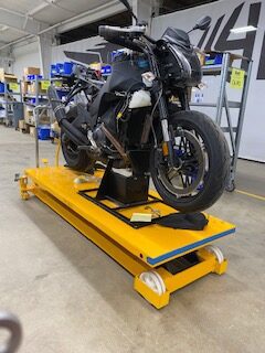 Custom black motorcycle on a yellow testing platform in workshop.