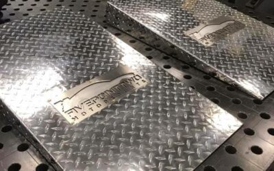 Two polished aluminum diamond plate panels on a workbench in a metal fabrication shop.