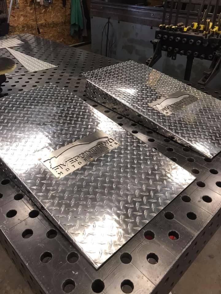 Two polished aluminum diamond plate panels on a workbench in a metal fabrication shop.