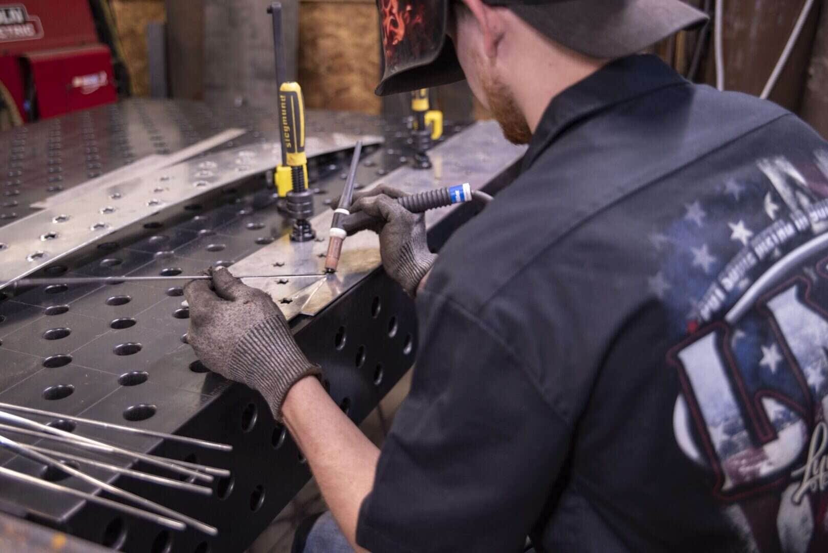 Worker welding metal with tools on a perforated metal surface.