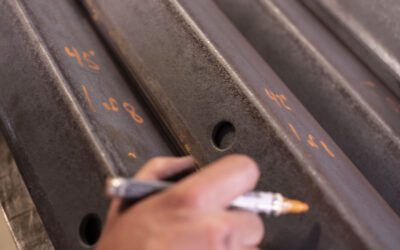 Worker marking metal beams with a pen in a fabrication shop.