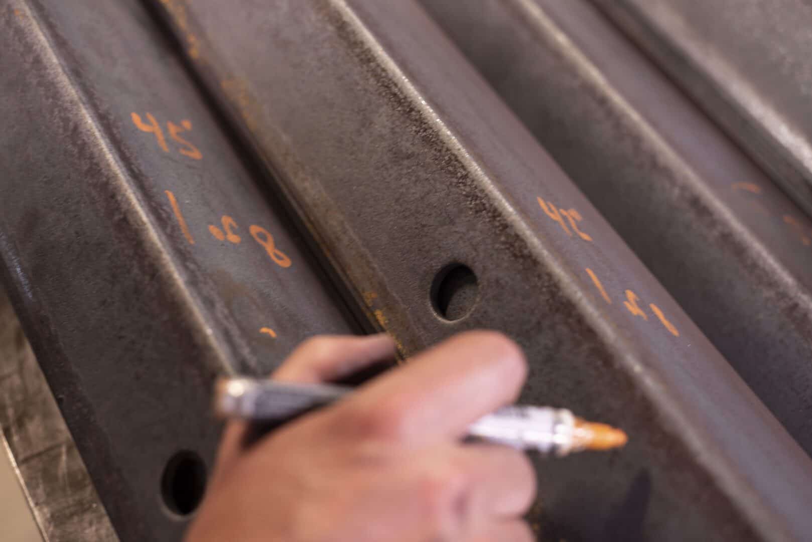 Worker marking metal beams with a pen in a fabrication shop.
