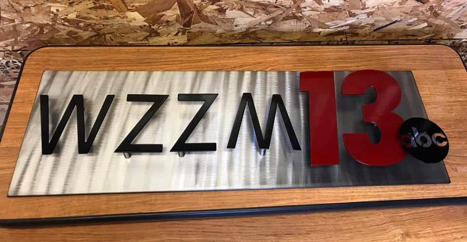Metal sign with WZZM 13 and ABC logo on a wooden surface.