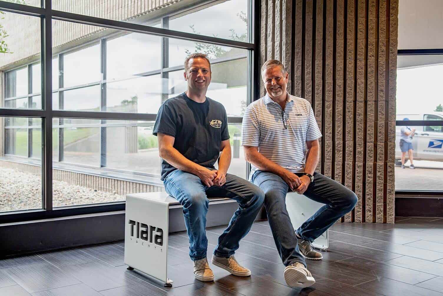 Two men sitting inside Lynch's Metal Fab office near large windows.