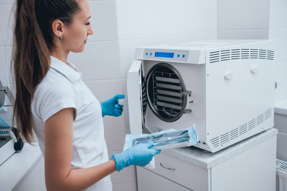 Mitarbeiterin legt verpackte Instrumente in einen Tischautoklaven zur Sterilisation.
