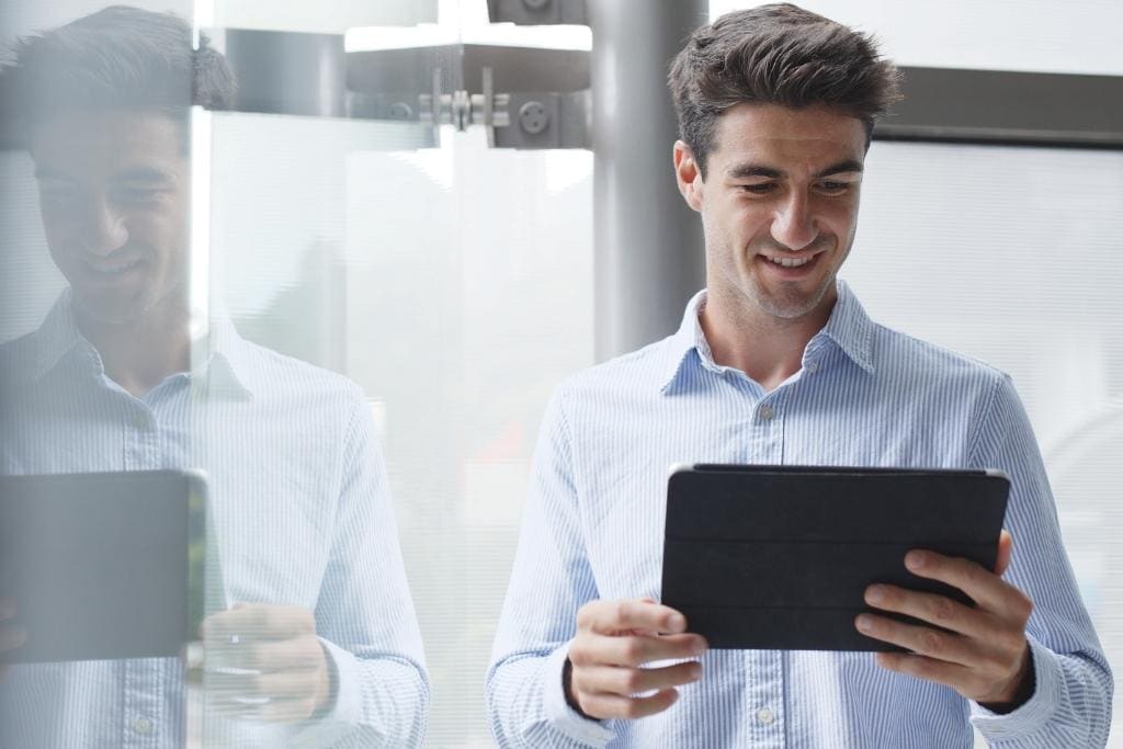 Ein lächelnder Mann im gestreiften Hemd hält ein Tablet für die digitale Anamnese in den Händen.
