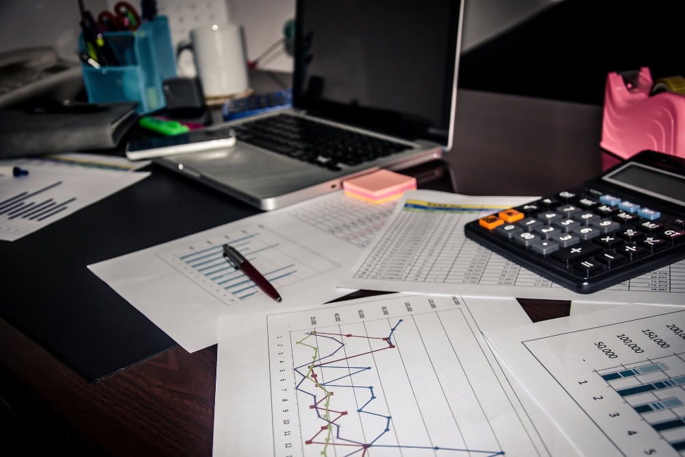 Schreibtisch mit Taschenrechner, Laptop und Dokumenten, die verschiedene Geschäftsdiagramme und Analysen für eine Praxisfinanzierung zeigen