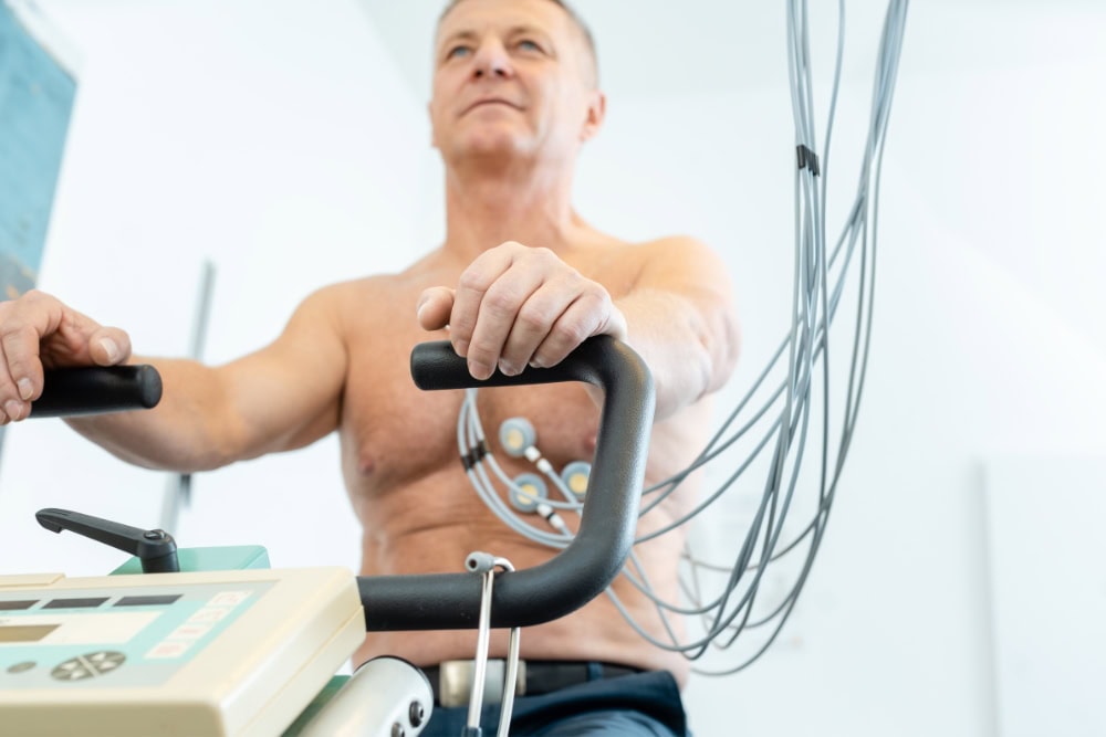 Patient sitzt während Belastungs-EKG (Ergometrie) auf einem Fahrradergometer
