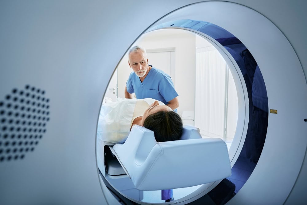 Eine Patientin wird für ein CT-Thorax-Abdomen in ein CT-Gerät geschoben. Arzthelfer führt CT-Untersuchung des Thorax bei Patientin durch
