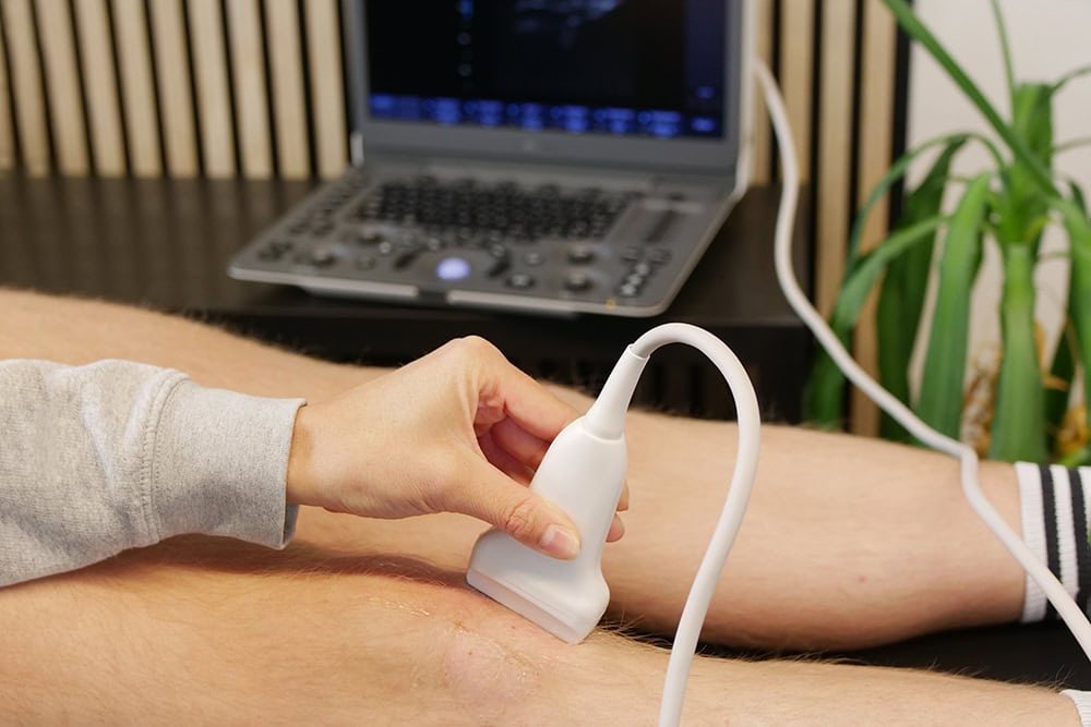 Ein Knie wird mit einem mobilen Laptop-Ultraschallgerät für die Orthopädie untersucht. Ein Knie wird mit einem mobilen Laptop-Ultraschallgerät für die Orthopädie untersucht.