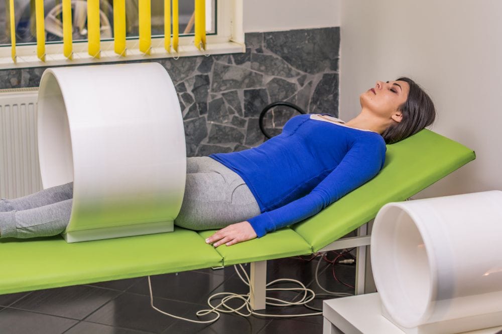 Eine Patientin liegt in einer Magnetröhre und lässt eine Magnetfeldtherapie an ihren Beinen durchführen. Magnetfeldtherapie der Beine in einer Magnetröhre