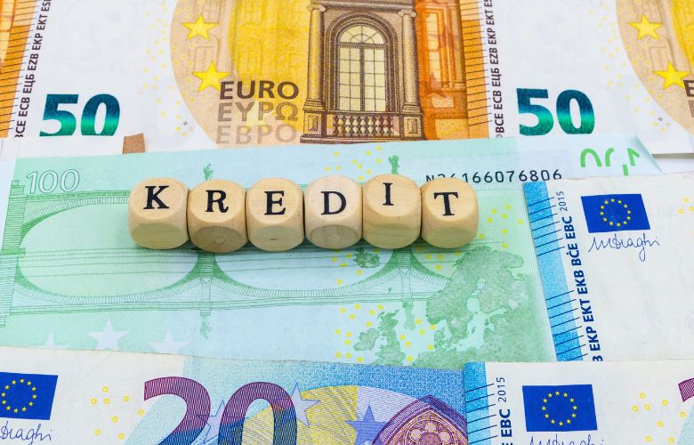 Holzbuchstaben mit dem Wort 'Kredit' auf Euro-Geldscheinen – Symbol für Praxiskredit