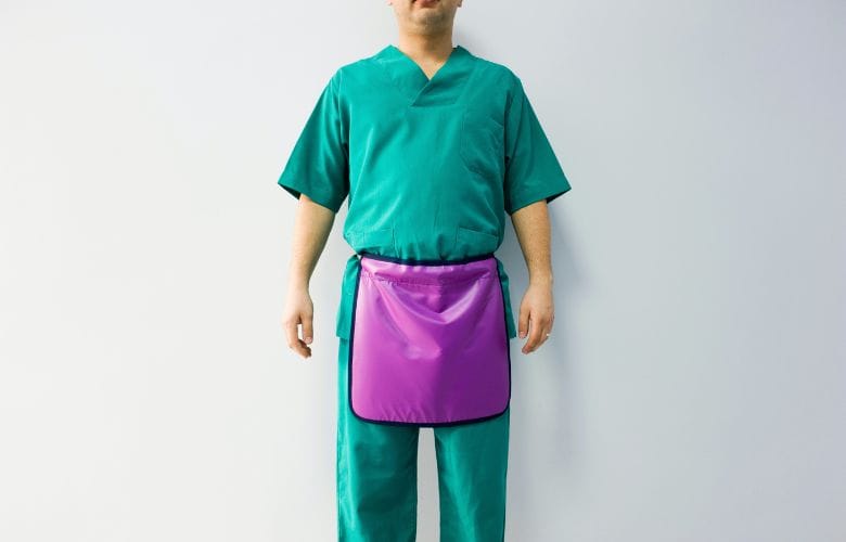 Ein Mann in grüner medizinischer Kleidung trägt eine violette Gonadenschürze, um sich beim Röntgen vor Strahlung zu schützen.