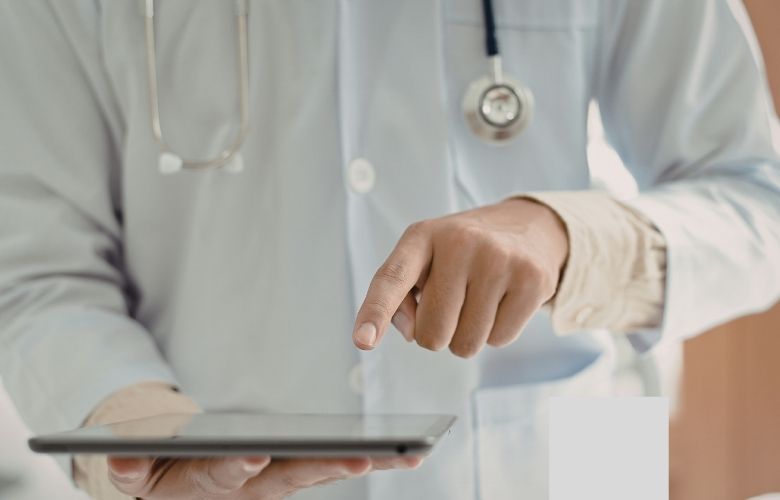 Ein Arzt im weißen Kittel mit Stethoskop bedient ein Tablet zur digitalen Patientenkommunikation.