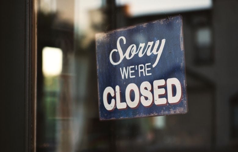 Blaues Vintage-Schild mit der Aufschrift "Sorry WE'RE CLOSED" an einer gläsernen Eingangstür.