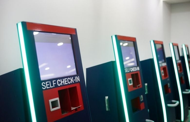 Mehrere dunkelblaue Self Check-In Terminals mit grünen Lichtleisten in einem hellen Praxisraum.