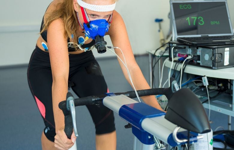 Sportlerin bei der Spiroergometrie auf einem Ergometer-Messplatz mit Atemmaske und EKG-Elektroden in einer Arztpraxis.