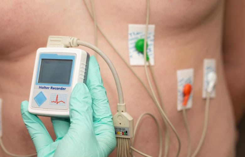Eine medizinische Fachkraft hält ein Holter-Langzeit-EKG-Gerät vor den auf dem Brustkorb fixierten Elektroden.