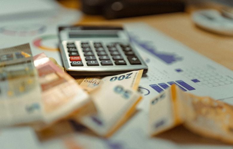 Euro-Banknoten und ein Taschenrechner auf Finanzgrafiken zur steuerlichen Planung einer Praxisgründung.