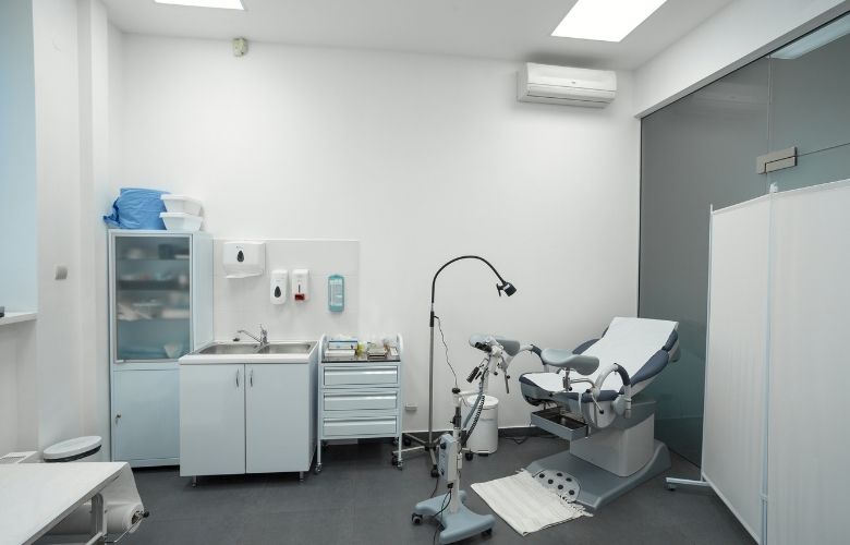Moderner Behandlungsraum einer Frauenarztpraxis mit Untersuchungsliege, medizinischen Instrumenten und Waschbecken.