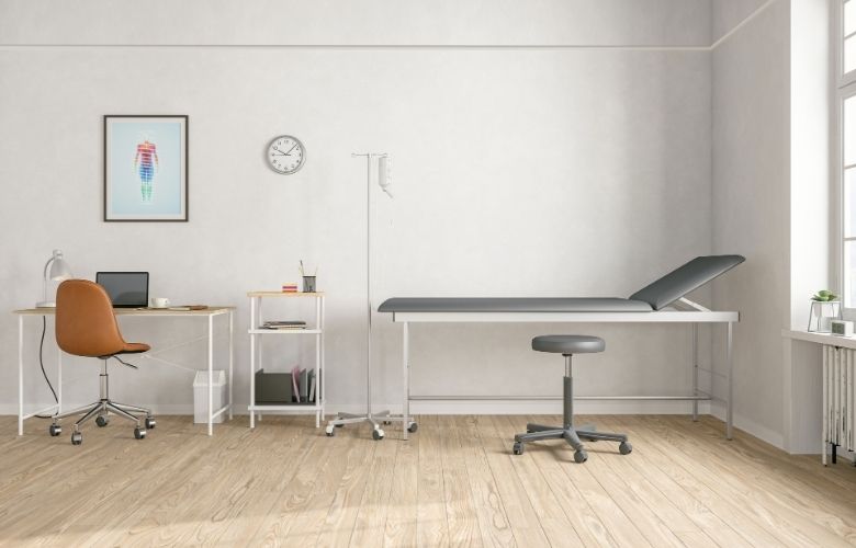 Moderne Praxiseinrichtung in einem hellen Untersuchungszimmer mit Behandlungsliege, Schreibtisch und Rollhocker.