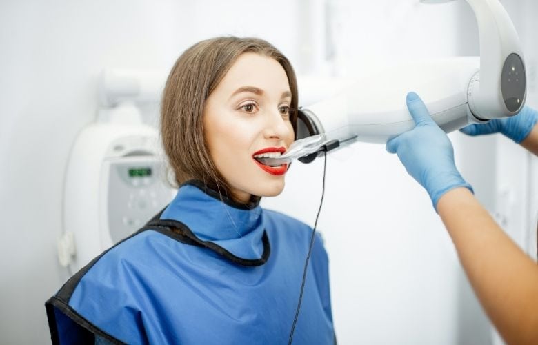 Eine Patientin mit Schutzschürze bei der Aufnahme mit einem intraoralen Röntgengerät in einer Zahnarztpraxis.