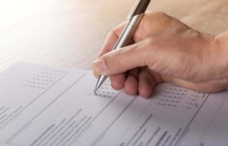 Eine Hand füllt mit einem Stift einen Fragebogen zur Patientenbefragung aus und kreuzt ein Feld an.