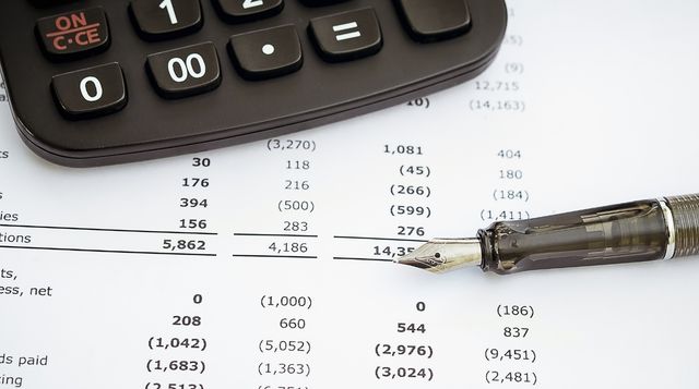Ein Taschenrechner und ein Füller auf einem Finanzdokument mit strukturierten Zahlenspalten.