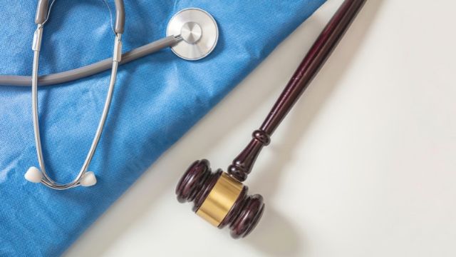 Ein Holzhammer eines Richters und ein Stethoskop liegen auf einem blauen medizinischen Tuch.
