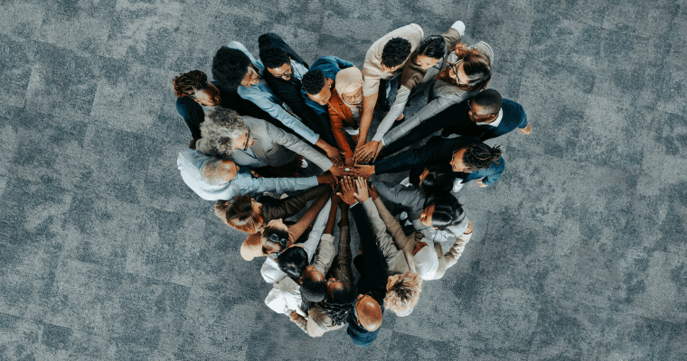 A diverse group of people form a heart with all of their hands touching from an aerial view.