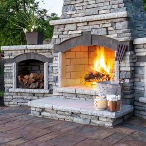 Outdoor stone fireplace with warm fire and decorative accessories.