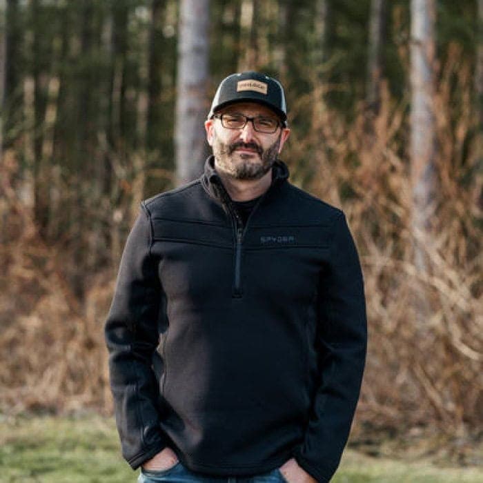 Man standing outdoors in a forest, representing team behind the website.